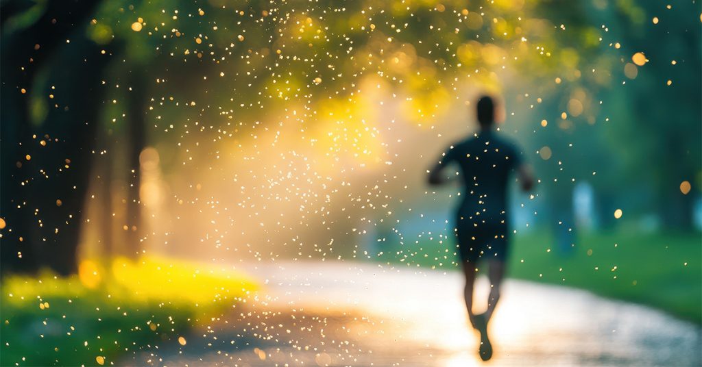 Silhouette of a man running, with sunshine lights up the pollen in the air.
