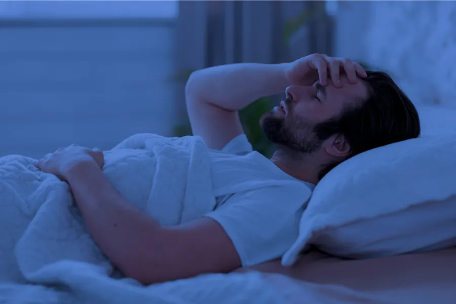 Man lying in bed with sinus discomfort and headache, showing sleep disruption from chronic sinus infection
